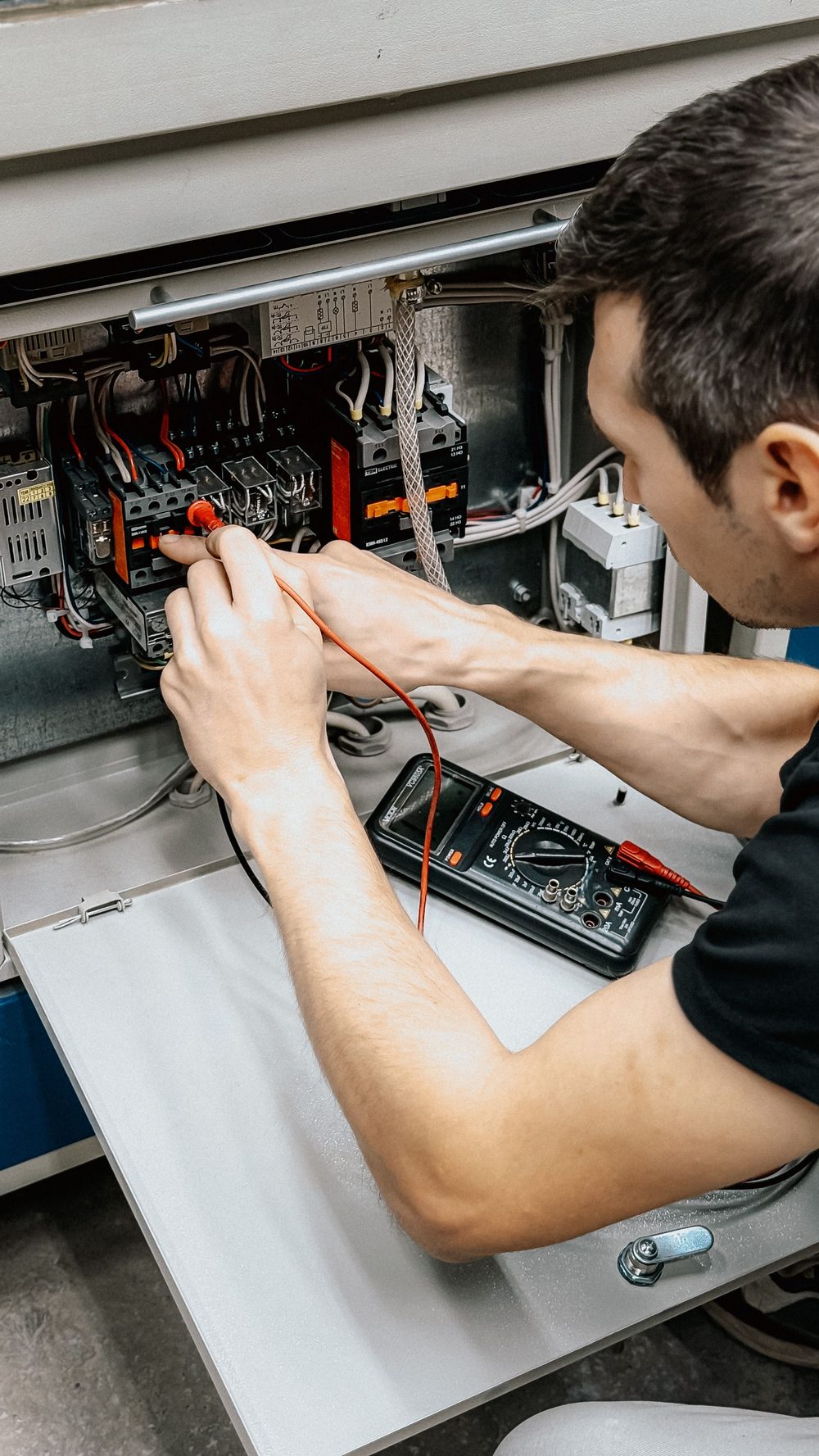 Technicien diagnostiquant une armoire électrique avec un multimètre